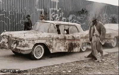A Black And White Photo Of A Man Standing Next To A Dirty Old Car . GIF