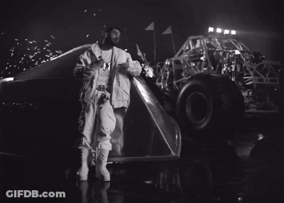 A Black And White Photo Of A Man Standing Next To A Monster Truck At Night GIF