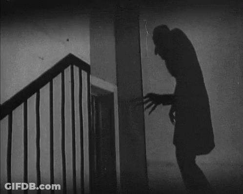 A Black And White Photo Of A Man Standing Next To A Staircase GIF