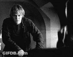 A Black And White Photo Of A Man Standing Next To A Wall Holding A Knife . GIF