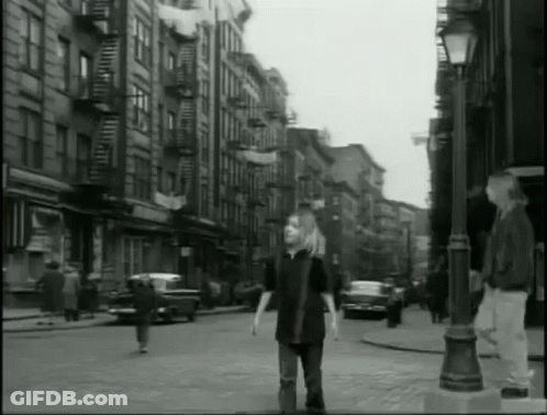 A Black And White Photo Of A Man Walking Down A City Street GIF
