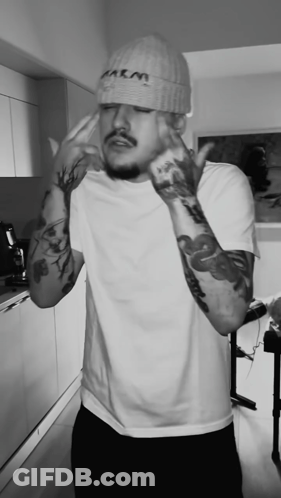 A Black And White Photo Of A Man Wearing A Beanie That Says M & M GIF