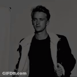 A Black And White Photo Of A Man Wearing A Black Jacket With A White Fur Collar GIF