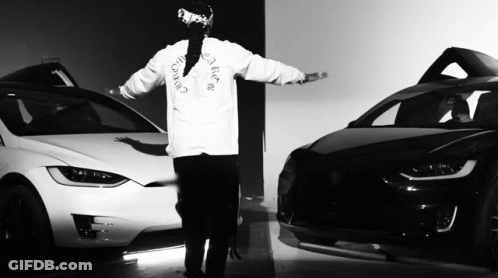 A Black And White Photo Of A Man Wearing A Christian Dior Shirt Standing Next To Two Cars GIF