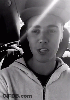 A Black And White Photo Of A Man Wearing A Hat And A Hoodie In A Car . GIF