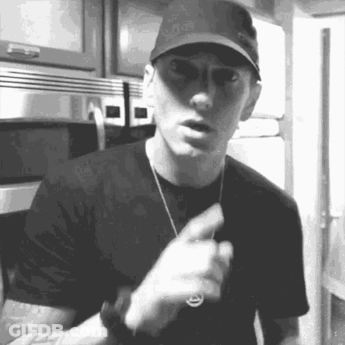 A Black And White Photo Of A Man Wearing A Hat And Sunglasses Pointing . GIF