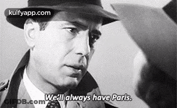 A Black And White Photo Of A Man Wearing A Hat And Tie Talking To Another Man . GIF