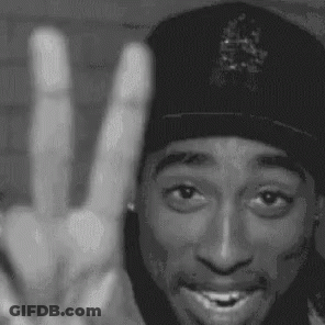 A Black And White Photo Of A Man Wearing A Hat Giving A Peace Sign . GIF
