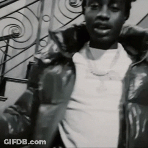 A Black And White Photo Of A Man Wearing A Jacket And A Necklace . GIF