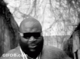 A Black And White Photo Of A Man Wearing Sunglasses And A Chain Around His Neck . GIF