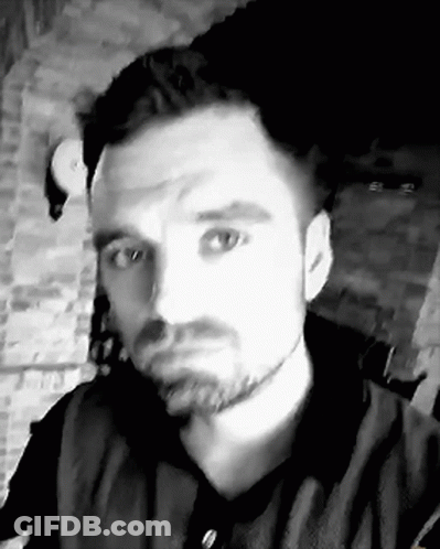 A Black And White Photo Of A Man With A Beard Taking A Selfie In Front Of A Brick Wall . GIF