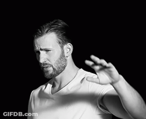 A Black And White Photo Of A Man With A Beard Wearing A White T-Shirt And A Necklace . GIF