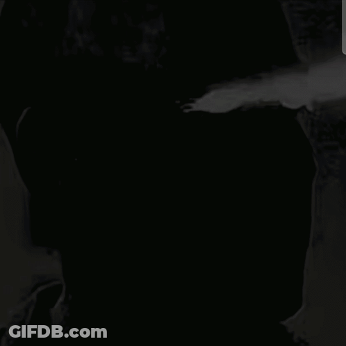 A Black And White Photo Of A Man With A Brick Wall Behind Him . GIF