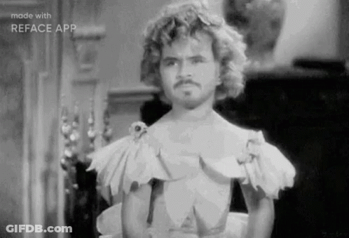 A Black And White Photo Of A Man With Curly Hair And A Mustache Wearing A Dress . GIF