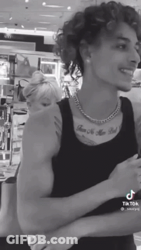 A Black And White Photo Of A Man With Curly Hair And A Tattoo On His Chest GIF