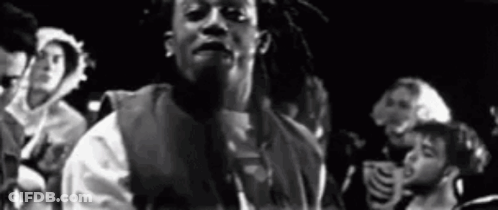 A Black And White Photo Of A Man With Dreadlocks Standing In Front Of A Crowd Of People . GIF