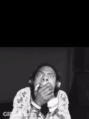 A Black And White Photo Of A Man With Headphones Covering His Mouth With His Hands GIF