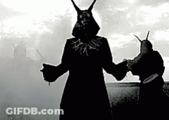 A Black And White Photo Of A Man With Horns Standing Next To Another Man GIF