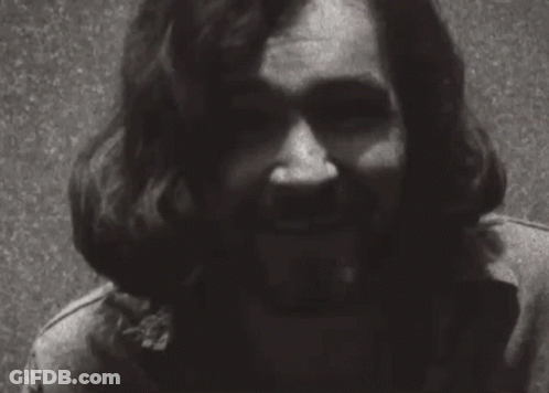 A Black And White Photo Of A Man With Long Hair And A Beard Smiling . GIF