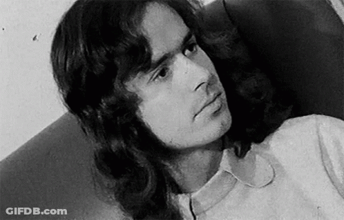 A Black And White Photo Of A Man With Long Hair And A White Shirt . GIF