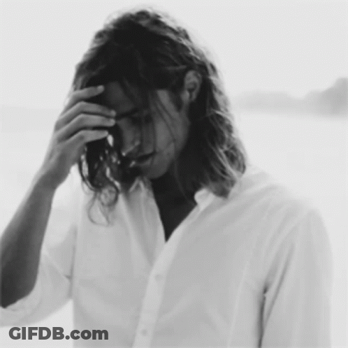 A Black And White Photo Of A Man With Long Hair Covering His Face GIF