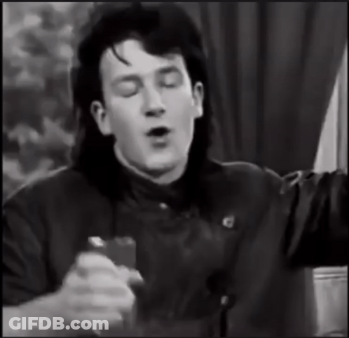 A Black And White Photo Of A Man With Long Hair Singing Into A Microphone GIF