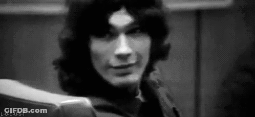 A Black And White Photo Of A Man With Long Hair Sitting In A Chair And Smiling . GIF