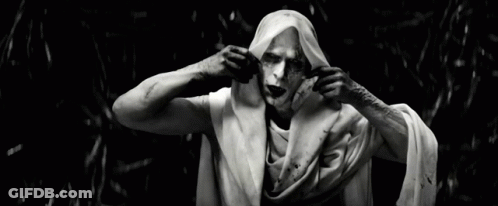 A Black And White Photo Of A Man With White Paint On His Face Holding A White Cloth Over His Head GIF