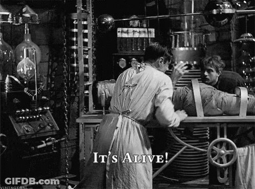 A Black And White Photo Of A Man Working On A Mummy With The Words It 'S Alive Below Him GIF