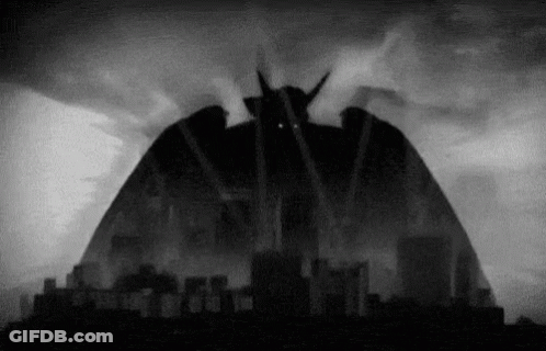 A Black And White Photo Of A Monster Coming Out Of The Sky Over A City GIF