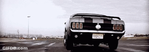 A Black And White Photo Of A Mustang Driving Down A Road . GIF