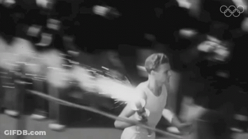 A Black And White Photo Of A Person Holding A Torch With The Olympic Symbol In The Background GIF