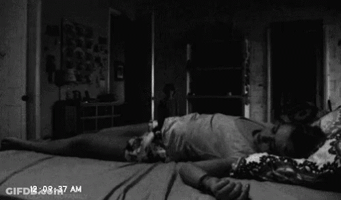 A Black And White Photo Of A Person Laying On Their Back On A Bed In A Dark Room . GIF