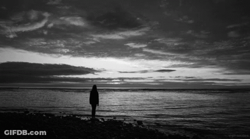 A Black And White Photo Of A Person Standing In Front Of A Body Of Water GIF
