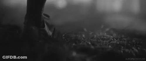 A Black And White Photo Of A Person Standing In The Grass With A Gun . GIF
