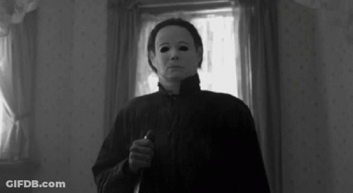 A Black And White Photo Of A Person Wearing A Mask Holding A Knife In A Room . GIF
