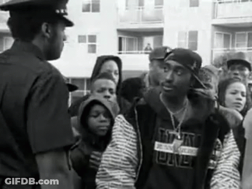 A Black And White Photo Of A Police Officer Talking To A Man In A Crowd . GIF