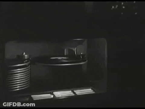 A Black And White Photo Of A Record Player And A Stack Of Records GIF