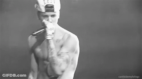 A Black And White Photo Of A Shirtless Man In A Baseball Cap Holding His Chest . GIF