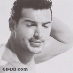 A Black And White Photo Of A Shirtless Man Smiling With His Arm Behind His Head . GIF