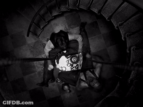A Black And White Photo Of A Spiral Staircase With Two People Laying On The Floor GIF