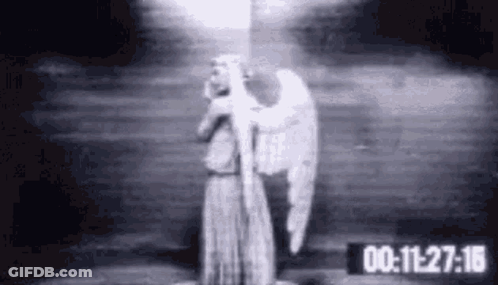 A Black And White Photo Of A Statue Of An Angel Holding A Light In A Dark Room . GIF