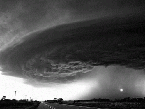 A Black And White Photo Of A Storm Over A Country Road GIF