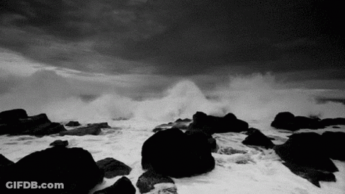A Black And White Photo Of A Stormy Ocean With Waves Crashing Against Rocks . GIF