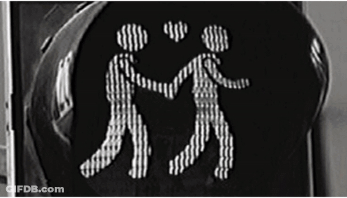 A Black And White Photo Of A Traffic Light With Two People Holding Hands GIF