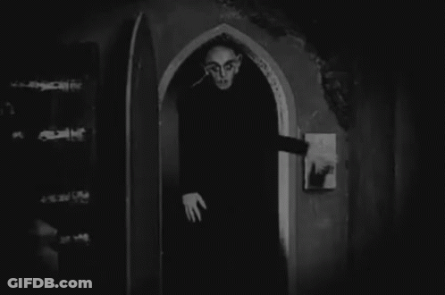 A Black And White Photo Of A Vampire Standing In An Archway . GIF