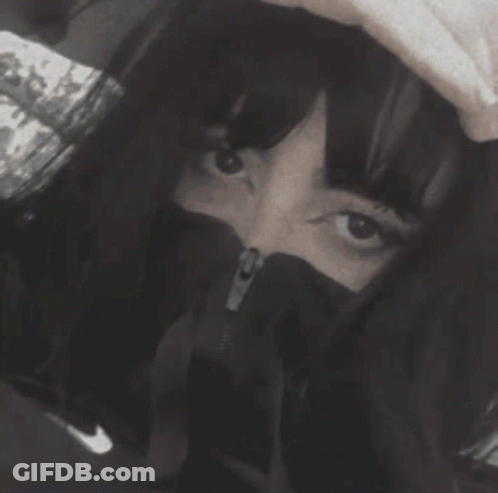 A Black And White Photo Of A Woman Covering Her Face With A Hood GIF