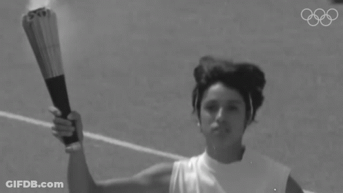 A Black And White Photo Of A Woman Holding A Torch With The Olympic Rings Behind Her GIF