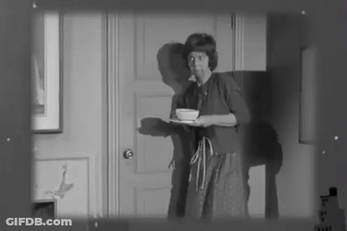 A Black And White Photo Of A Woman Holding A Tray With A Bowl On It GIF
