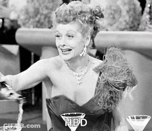 A Black And White Photo Of A Woman In A Dress Sitting At A Table With A Martini . GIF